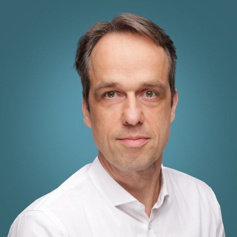 Praxisarzt Holger Nückel , Neutral gekleideter Mann mit kurzem Haar und einem ernsthaften Blick vor einfarbigem Hintergrund.