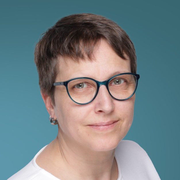 Frau mit Brille und kurzen Haaren, in einem weißen Oberteil, vor blauem Hintergrund.